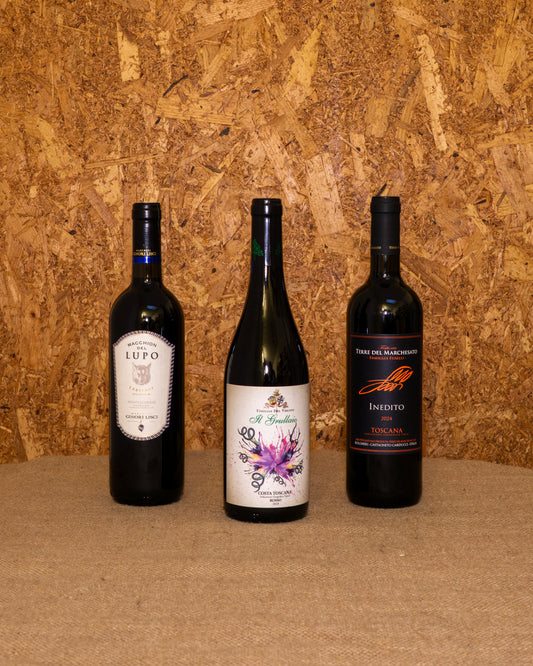 Le 3 bottiglie della selezione «Toscana Rossa» in piedi davanti al fondo del set: Grullaio Costa Toscana IGT, Montescudaio DOC “Lupo” e Inedito Terre del Marchesato.