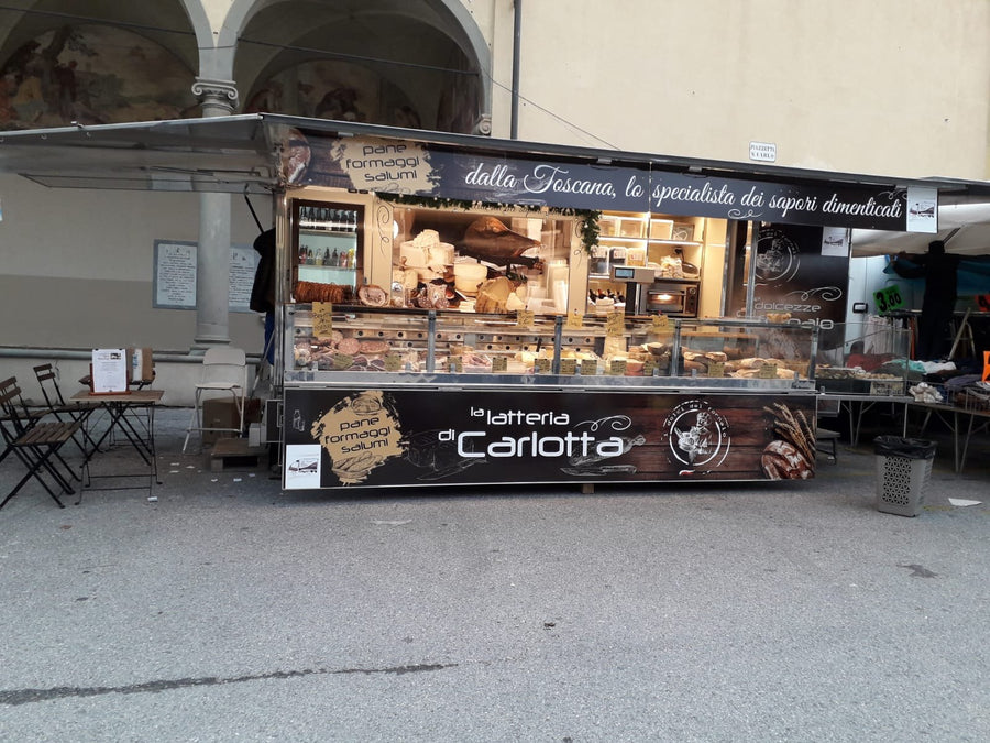 L'autonegozio de La Latteria di Carlotta aperto sotto un loggiato, col banco refrigerato e l'insegna dei sapori dimenticati della Toscana