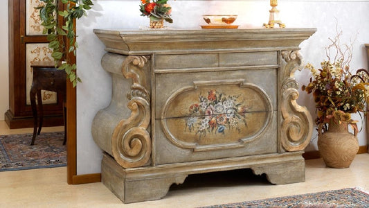 La credenza chiusa vista di fronte: il piano che sporge, l'ovale dipinto e il basamento sagomato