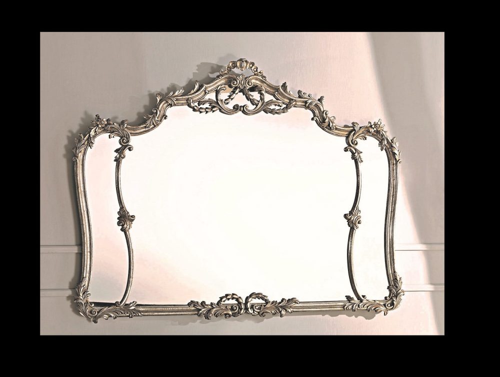 The 1575 mirror: the carved crest at the centre and the corner ornaments at the angles, with the thin profile between one and the other