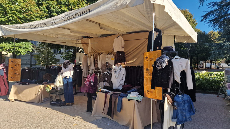Il banco Le Griffes di Carmen al mercato: il tendone col nome in corsivo, gli stendardi arancioni, gli stender dei capi e i tavoli