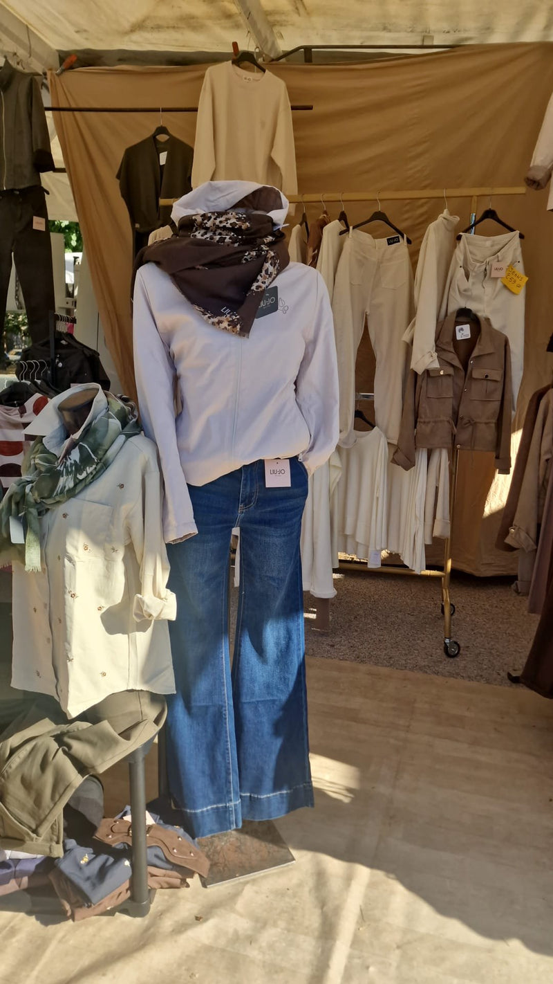 Un manichino con jeans a zampa, maglia chiara e foulard, davanti agli stender del banco