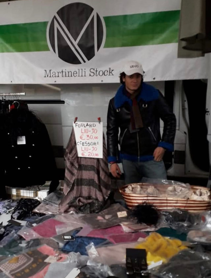 L'insegna Martinelli Stock sopra il banco, con i capi appesi e il tavolo davanti