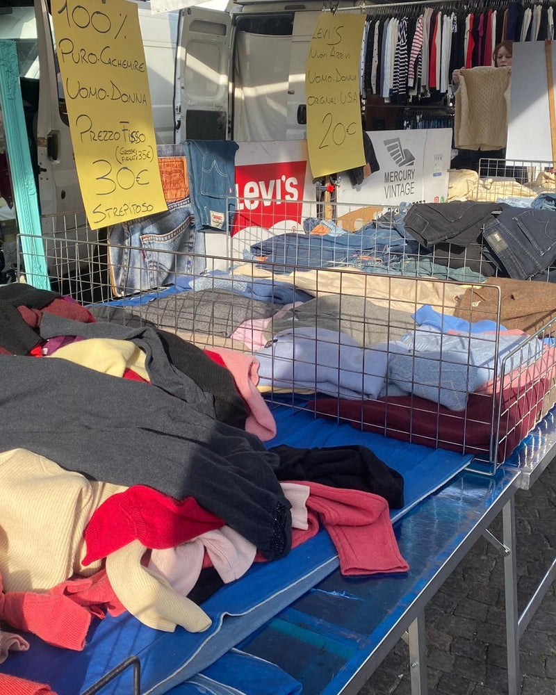 Maglioni piegati e jeans sul banco di Mercury Vintage, con due cartelli dei prezzi scritti a mano