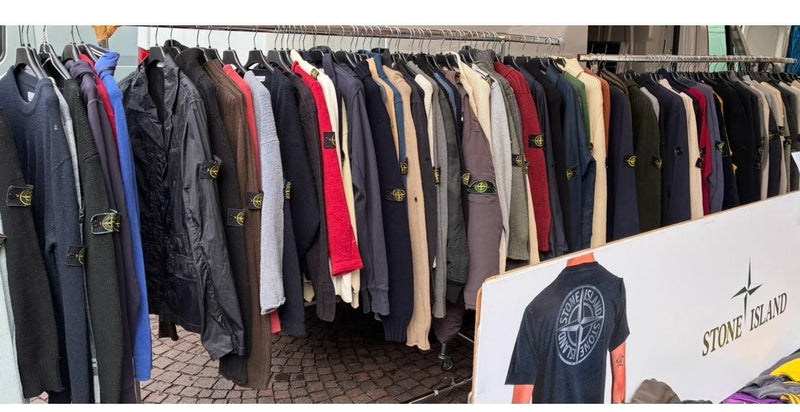 Una fila di giacche e maglioni appesi, con un cartellone pubblicitario accanto