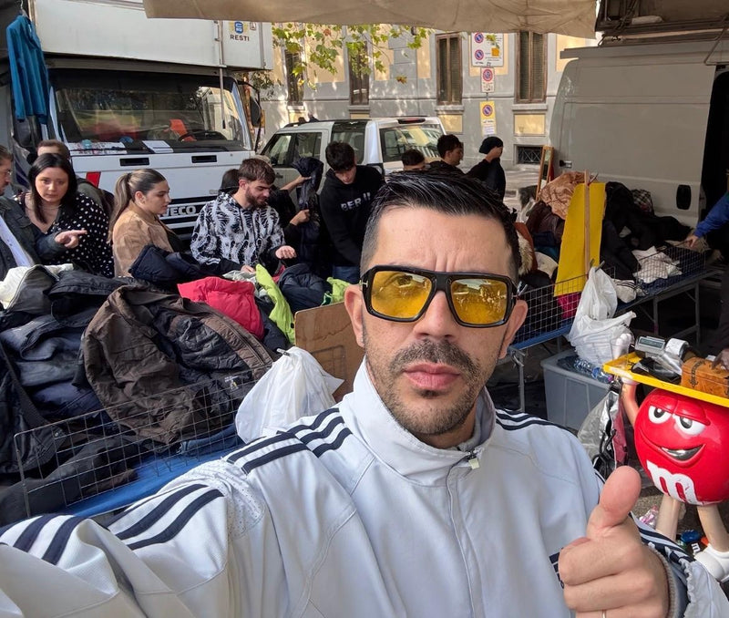Selfie di Luca Carlesi al banco, pollice in su, con i clienti che scelgono fra le giacche alle sue spalle