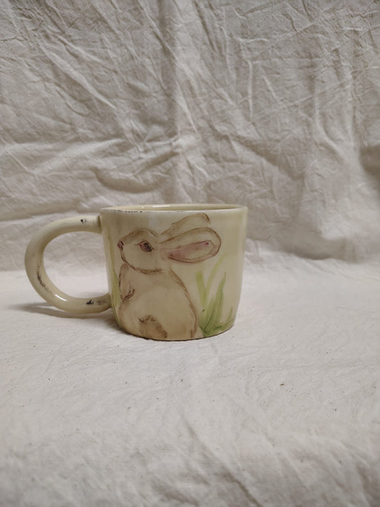 Tazza con un coniglio bruno seduto nell'erba