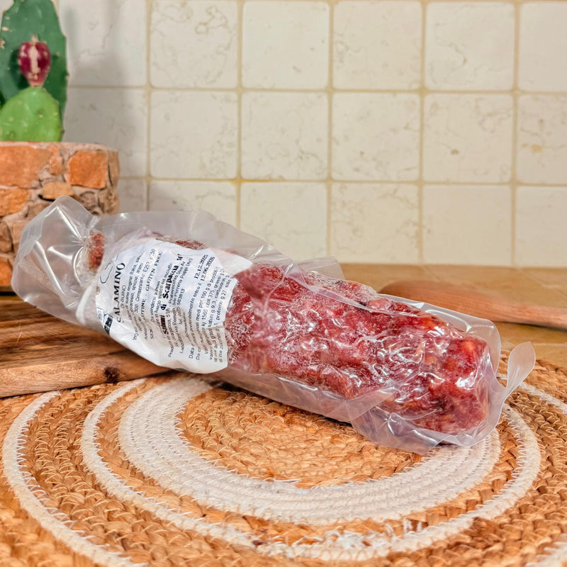 Il salame intero sottovuoto, appoggiato sul centrino all'uncinetto