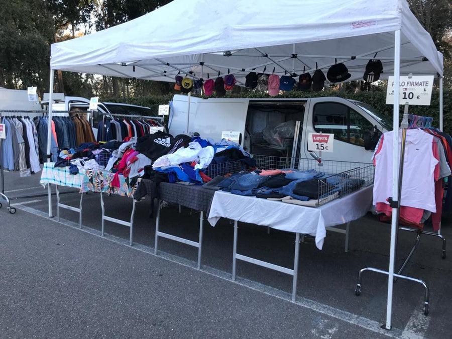 Il banco di Marco Raugei al mercato: il gazebo bianco, gli stender dei capi e il tavolo dei jeans, con i cartelli dei prezzi scritti a mano